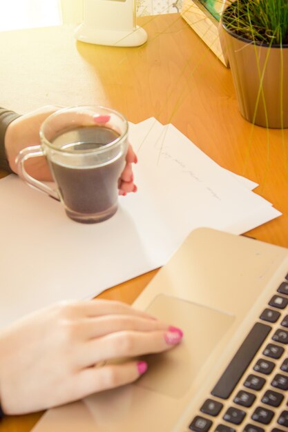 A close-up shot of a hand filling out an unemployment benefits application form with a pen. The form is on a desk along with a laptop and a cup of coffee.