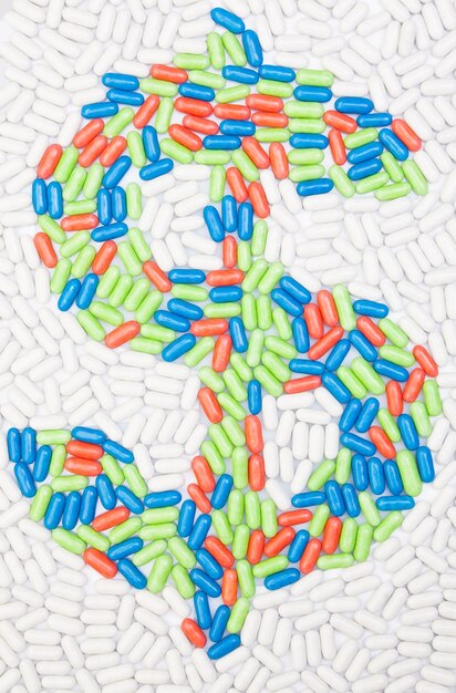 A close-up shot of prescription pills in various colors and shapes, arranged to form the shape of a dollar sign.