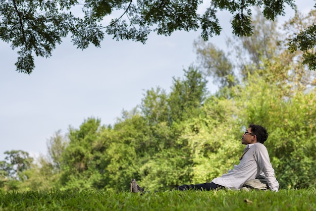 A person meditating outdoors in a peaceful, sunny park. They are sitting cross-legged on a yoga mat, eyes closed, with trees and greenery surrounding them, conveying a sense of calm and mindfulness.