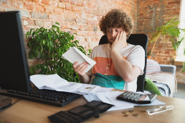 A stressed individual sitting at a desk, surrounded by bills and financial documents, conveying the burden of financial stress.
