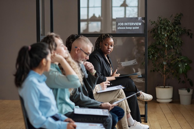 A diverse group of people attending a seminar about starting a side hustle, with a presenter pointing to a slide about government grants. The room is filled with eager participants taking notes.
