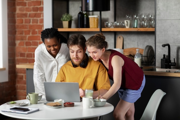 Three people collaborating around a table, working on a web design project on a laptop. The setting is informal, suggesting a dynamic team environment.