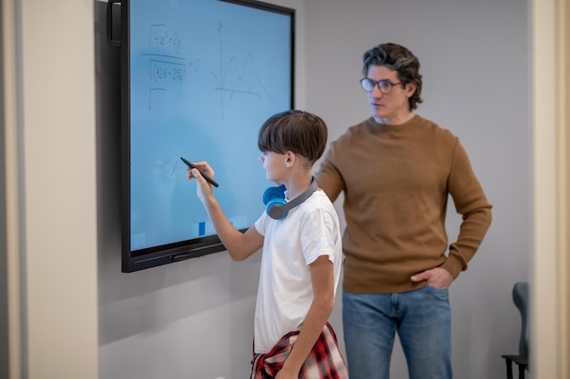 A tutor is teaching a student online, using a shared digital whiteboard for a math problem. Both are focused on the screen, with tools like pens and erasers visible on the whiteboard interface.