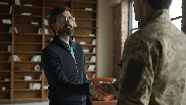 A US military veteran shaking hands with a hiring manager in a modern office environment. Both are smiling and engaged in conversation, symbolizing a successful job interview and the smooth transition of veterans into civilian employment. The office setting is bright and professional, representing the career opportunities available to veterans.