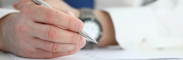 A close-up of a hand signing a time sheet with a pen, with a calculator and stacks of documents in the background, symbolizing accurate tracking of work hours and compensation compliance.