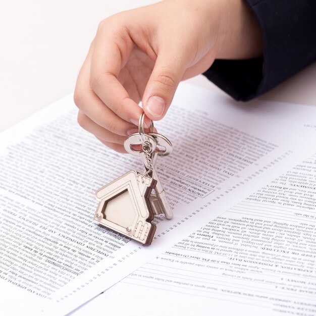 A close-up of a hand holding a key over a contract with financial charts and graphs in the background, symbolizing the connection between interest rates and homeownership.