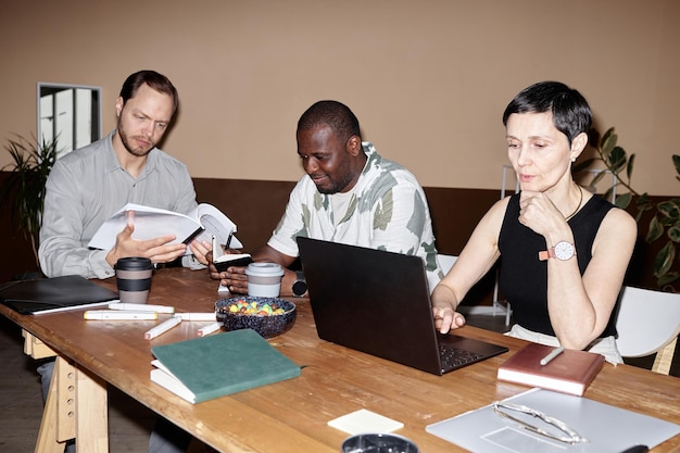 A diverse group of people gathered around a table working on laptops and papers, appearing to collaborate on a grant application. The atmosphere is bright and focused, with a sense of determination.