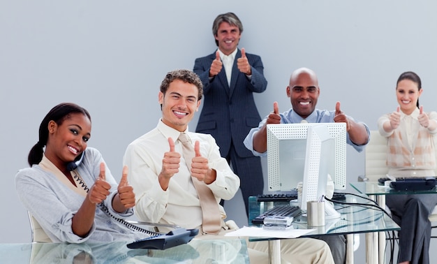 A diverse group of employees gathered in an office setting, smiling and giving a thumbs up, representing workplace retirement plans and financial benefits.