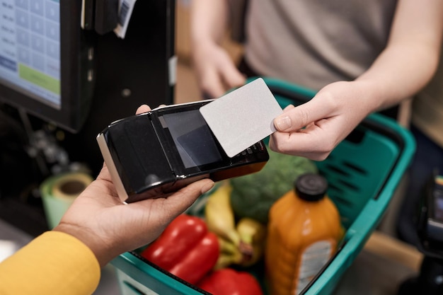 A close-up of an EBT card being used at a grocery store checkout. The focus is on the card and the point-of-sale terminal, with a blurred background showcasing various food items.