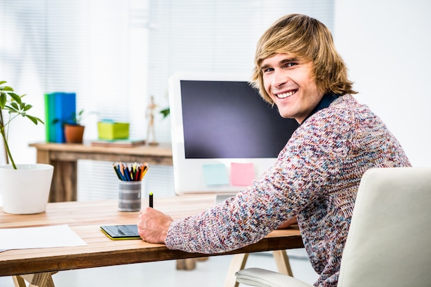 A person sitting at a desk, smiling and confidently using budgeting software on a laptop, with a notebook and pen nearby.